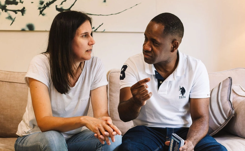 A couple have a conversation while sitting on a sofa.