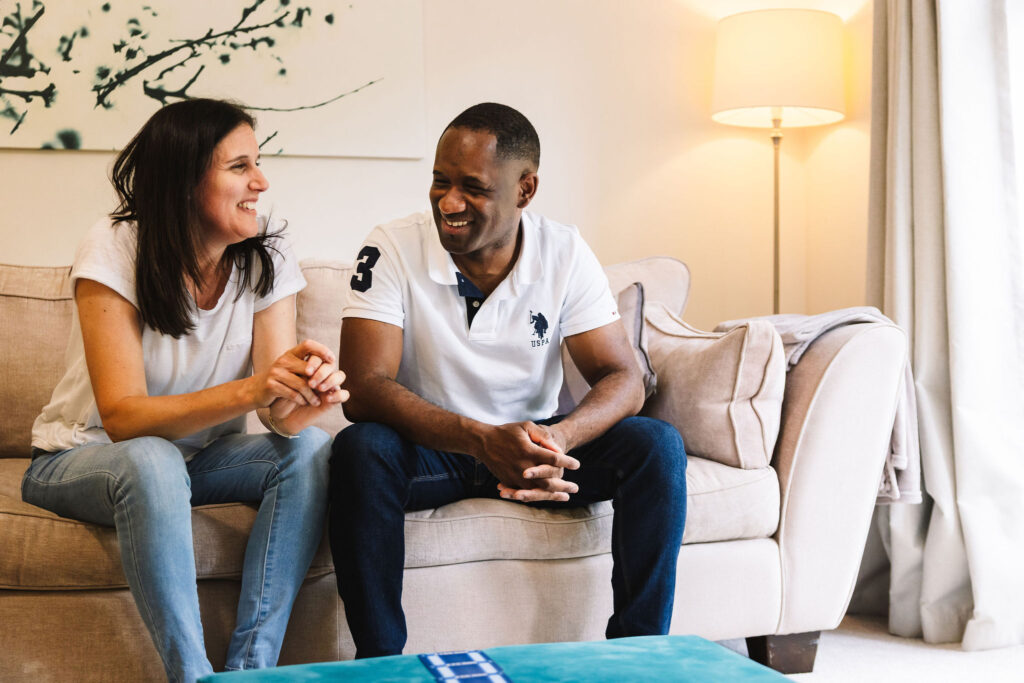 A couple sitting next to each other on a sofa laughing.