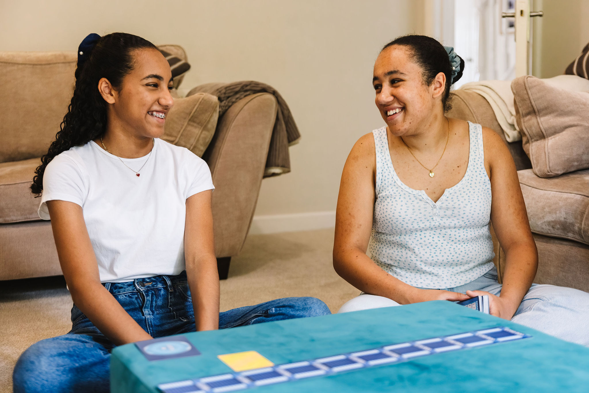 Two teenage sisters laugh together while paying a card game.