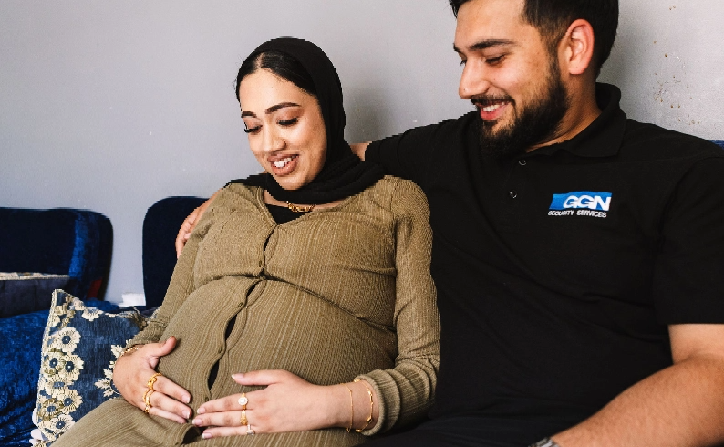 An expectant mother holding her pregnancy bump while sitting with her partner.