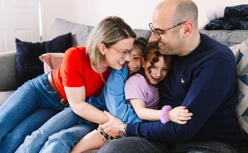 A mother, father and their daughters share a group hug.