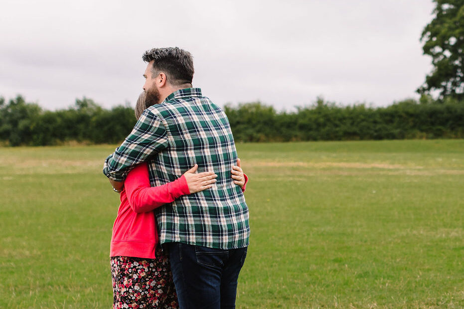 Two adults, a man and a woman, hug each other outside.