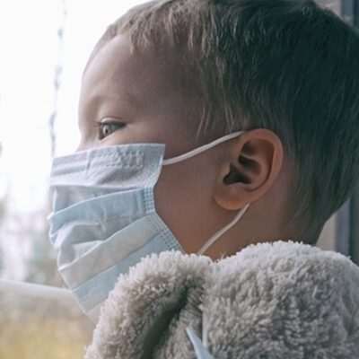 A young boy wearing a face mask looks out of a window.