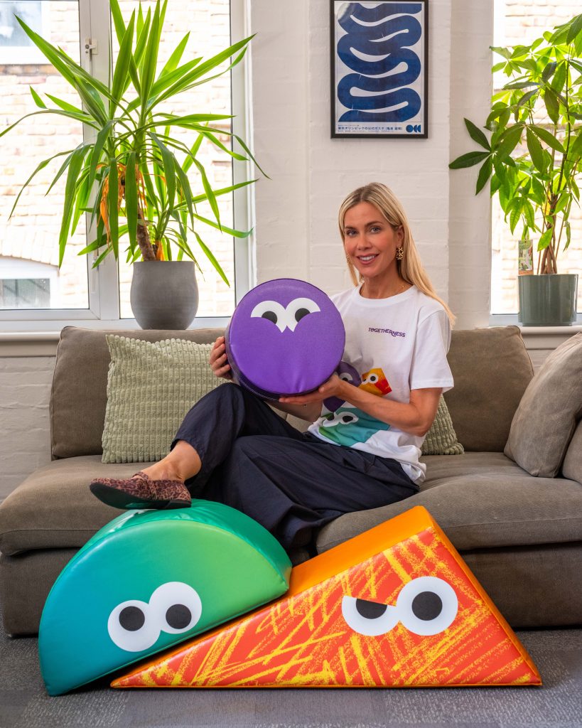 Kate Lawler sits on a grey sofa with Togetherness' soft play shapes.