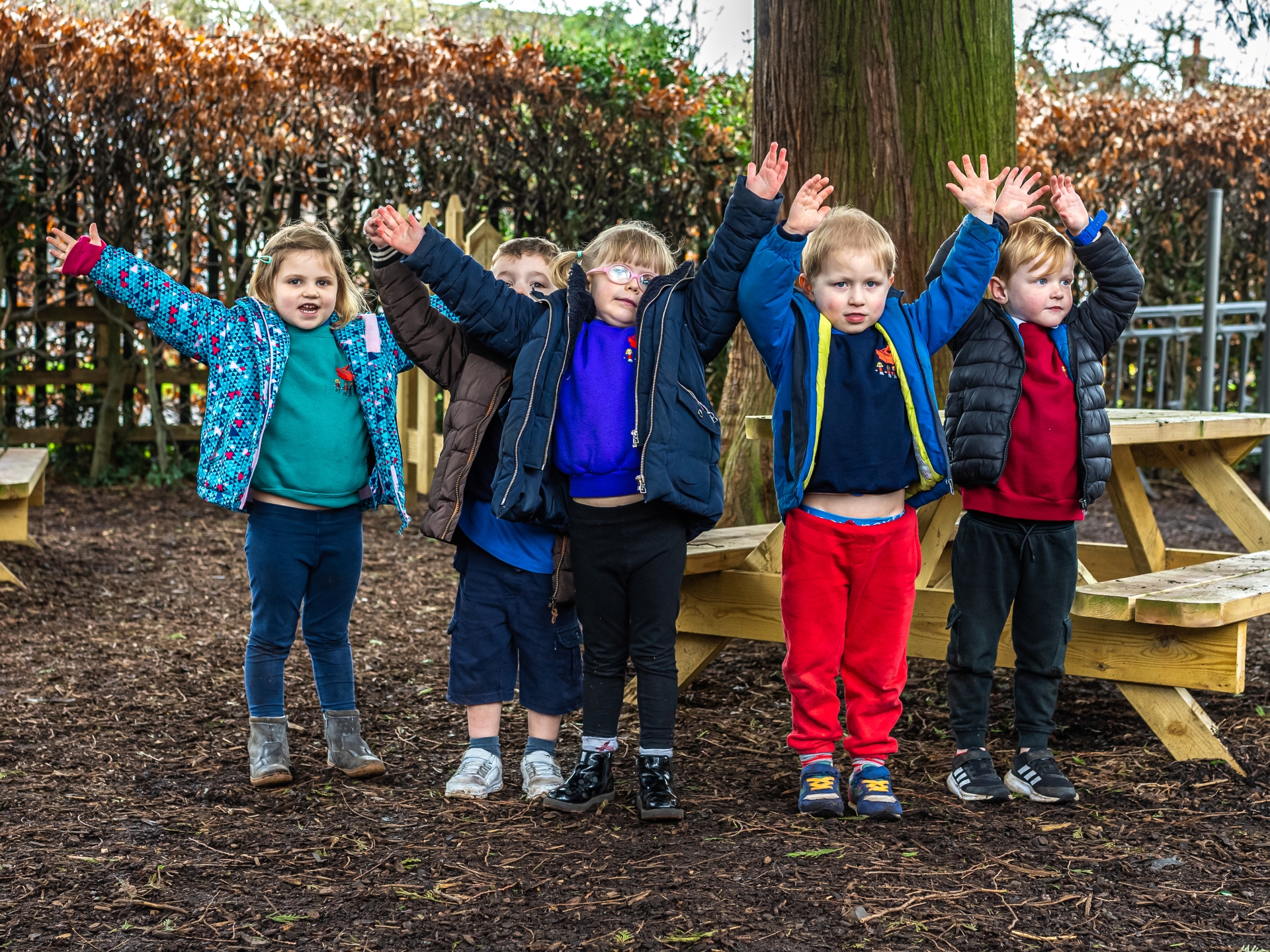 Five children aged four and five smiling with their hands in the air.